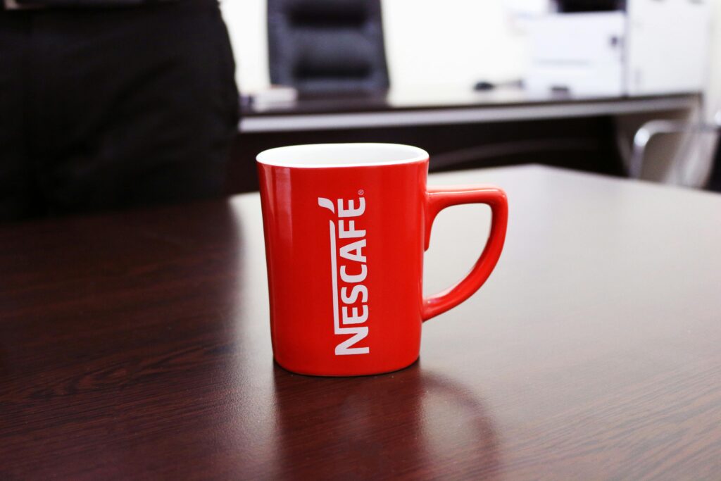 Red Nescafé mug on wooden desk in office setting, perfect for coffee-themed content.